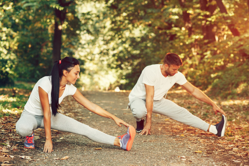 The man and the woman take a moment, together, to stretch out their legs to prevent hip pain after running