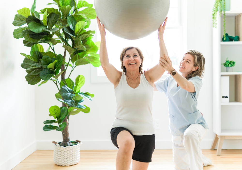 a mature woman practicing lunges with the help of a physical therapist, as a part of fall prevention physical therapy