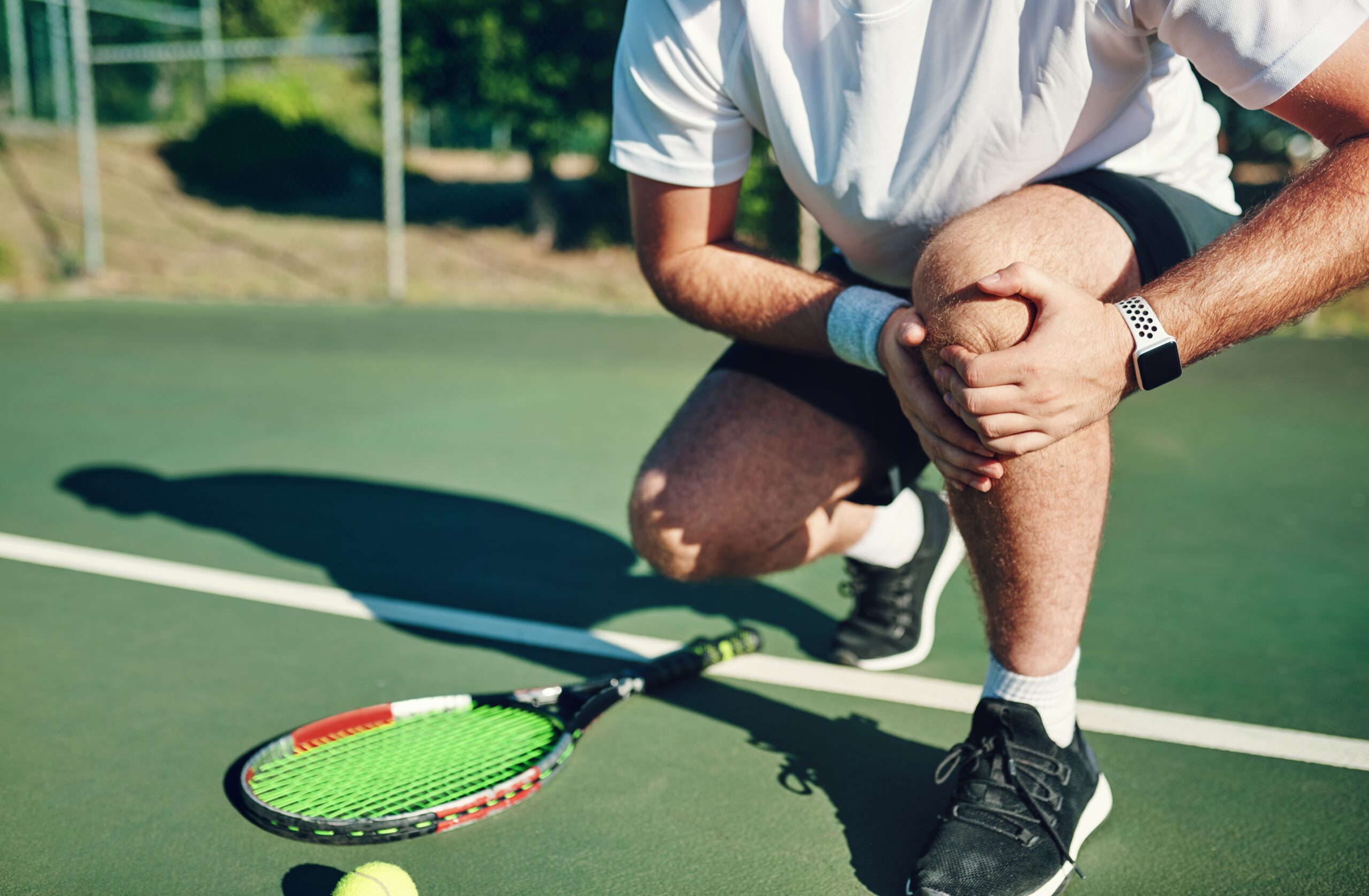 man clutching his knee in pain from a tennis injury
