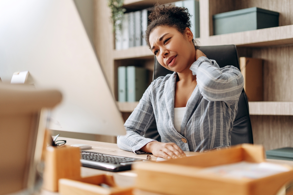 A woman experiencing neck pain from poor ergonomics at work.